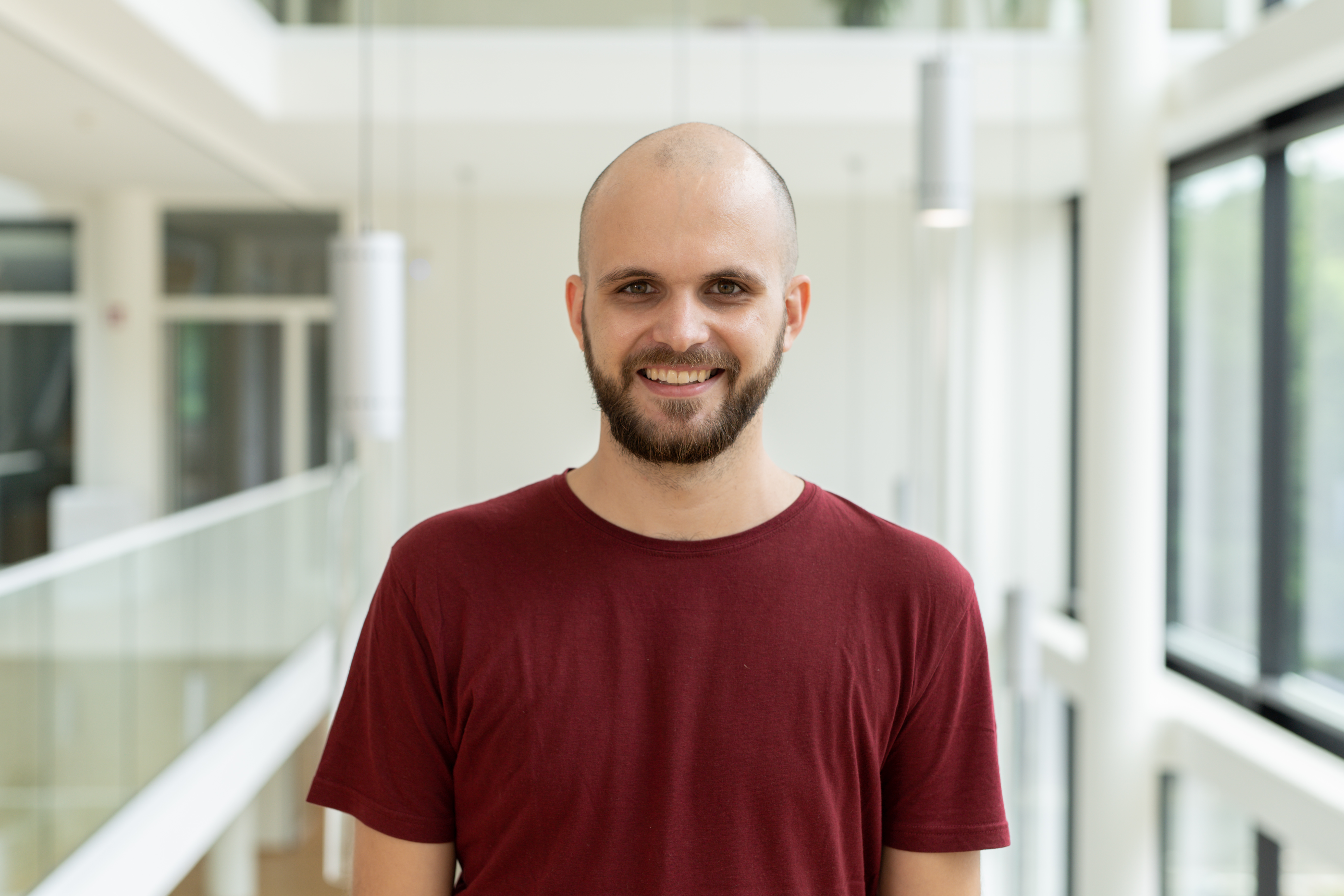 a European male with a bald head, short facial hair, and a red T-shirt
